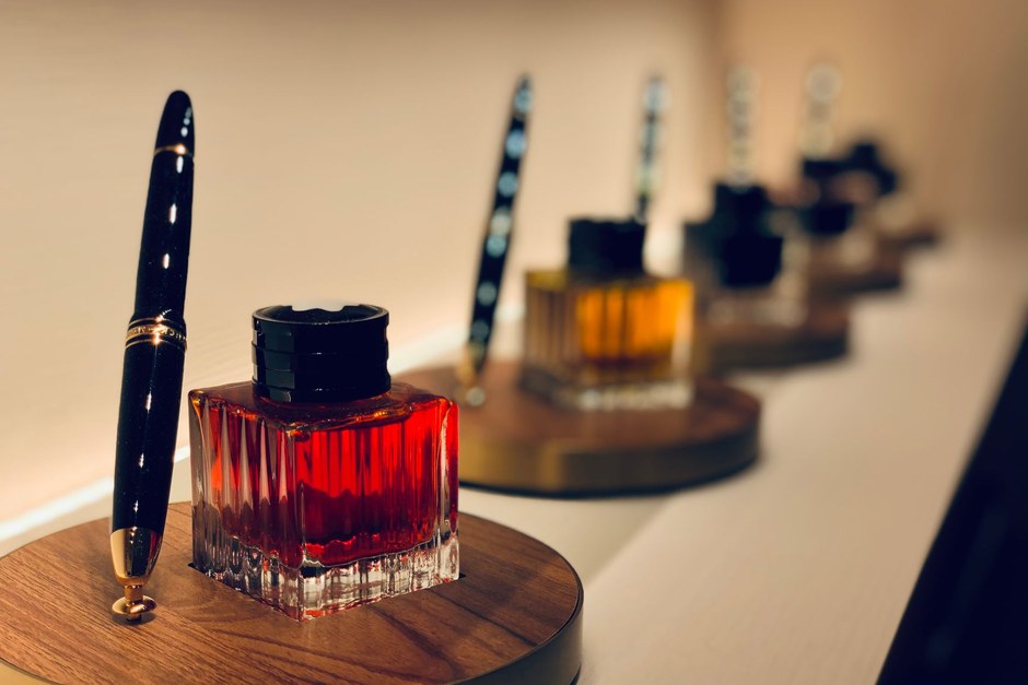 Glass bottles of red, amber and dark ink with fountain pens on wooden stands