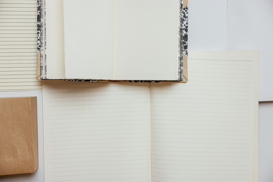 A blank notebook resting across open lined notebooks on a light surface