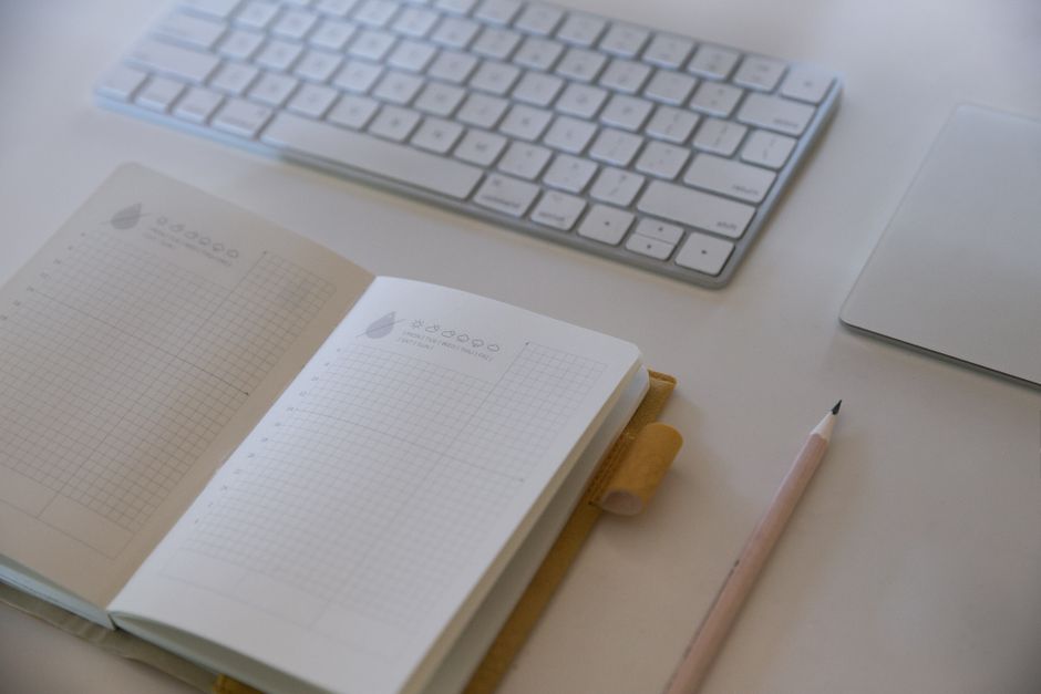 Open grid notebook and pencil beside a keyboard on a light desk